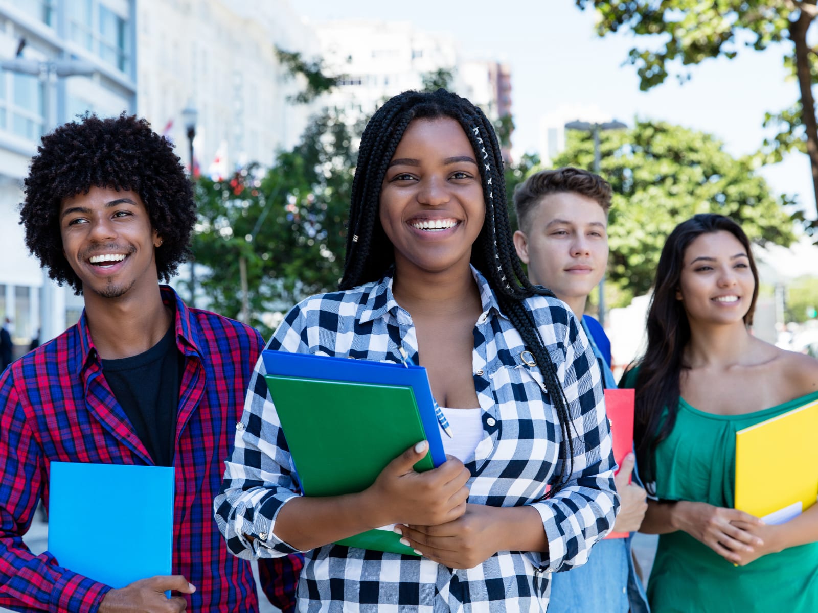 A smiling African student holding books outdoors with fellow students