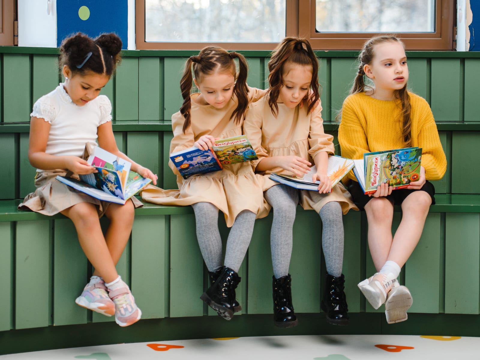 Young girls sitting on a bench, each reading a picture book